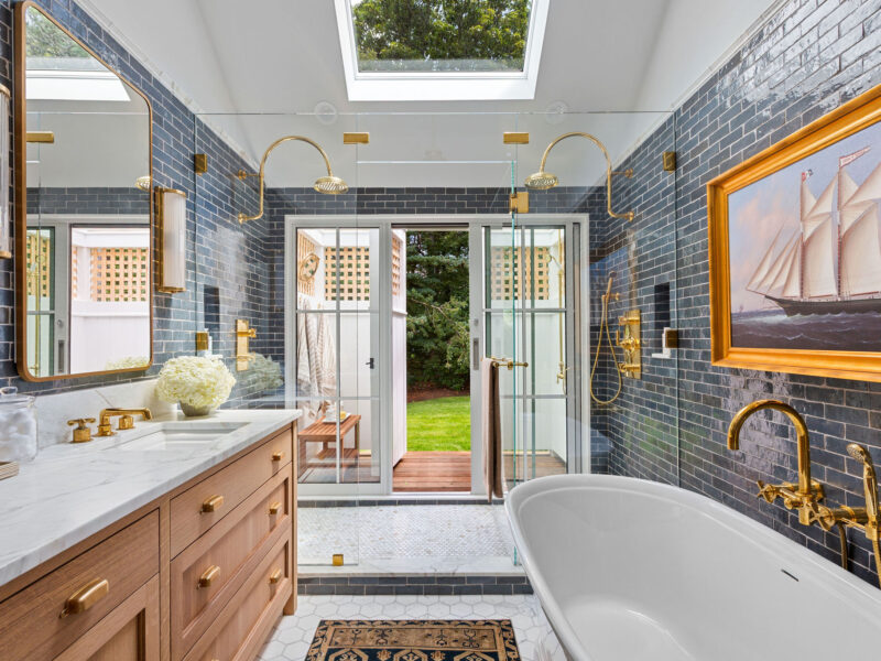 Blue subway tile walls, skylight, gold fixtures, double showerheads, and a sailboat painting – McPhee Associates of Cape Cod.